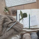 A calendar and sketchpad on top of a desk surrounded by knitting, tea, and a keyboard