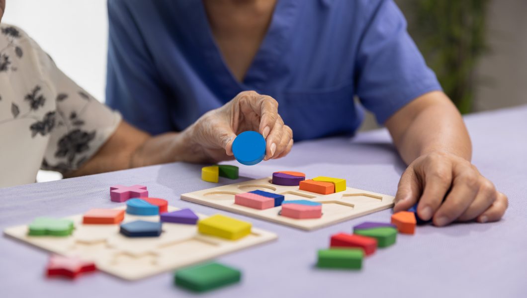 Caregiver and senior woman playing wooden shape puzzles game for dementia prevention