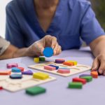 Caregiver and senior woman playing wooden shape puzzles game for dementia prevention