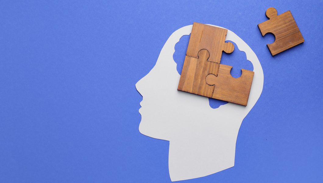 Paper human head and pieces of jigsaw puzzle on color background. Concept of dementia