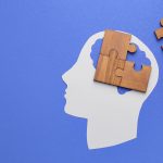 Paper human head and pieces of jigsaw puzzle on color background. Concept of dementia