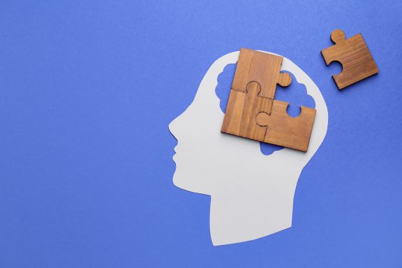 Paper human head and pieces of jigsaw puzzle on color background. Concept of dementia