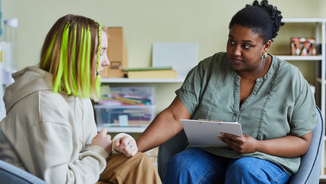 African female school psychologist supporting sad teenage girl during her difficult situation at school